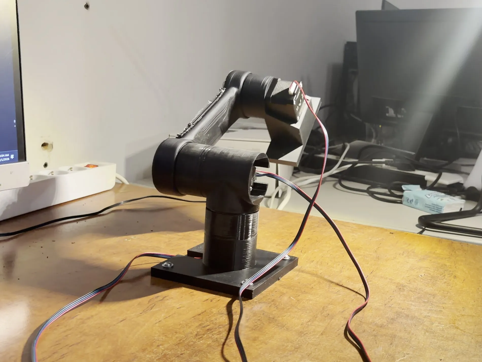 The arm on its base plate, three joints built, ribbon cable running down the side